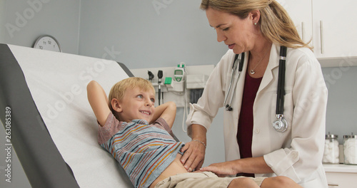 Female pediatrician performing regular check up on young boy in clinic exam room. Woman doctor giving exam to child in pediatrician office