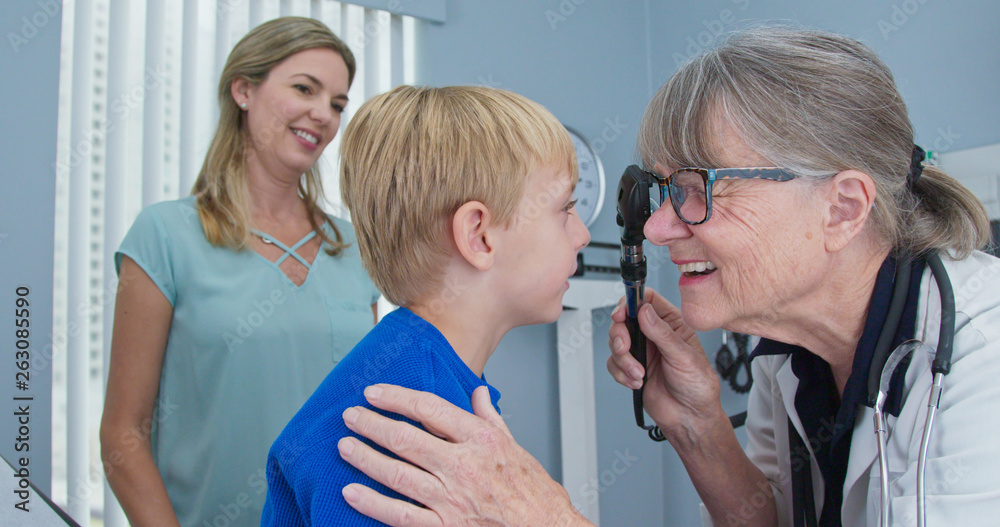 Friendly pediatrician performing eye exam using ophthalmoscope on child