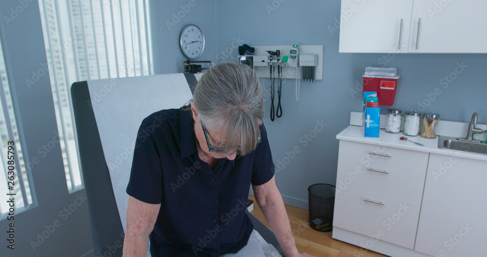 Obraz premium High angle view of Senior woman patient looking down while sitting in medical exam room waiting for the doctor. Older female in clinic or hospital waiting for primary care physician