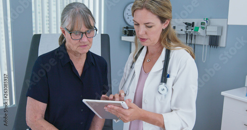 Female primary care doctor having conversation with older Caucasian woman during regular check up. Senior patient talking with her reassuring physician in exam room photo