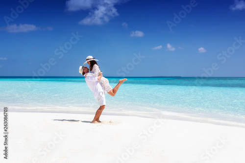 Happy, young couple in white summer clothes enjoying their vacation on a tropical beach