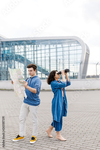 Young cute couple - a boy and a girl walking around the city with a map and binoculars in his hands. Young people travel.