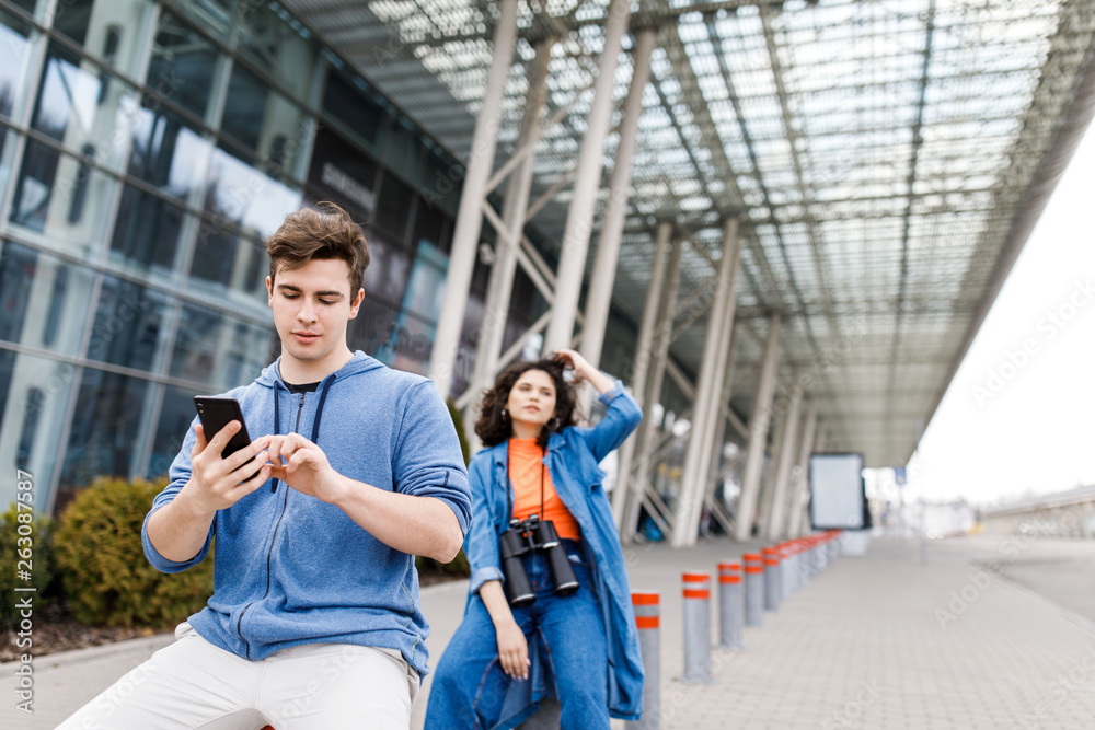 The guy holds the phone in his hands. Young cute couple - a boy and a girl travel around the city with binoculars in their hands. Young people travel.