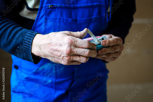 A builder in an orange building mask in his hands with a sandpaper holder. Blue form combining. Repair in the apartment.
