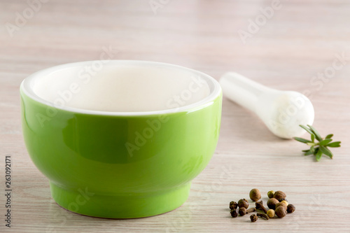 Green ceramic mortar and pestle with spilled mixture of pepper beans at the vintage background