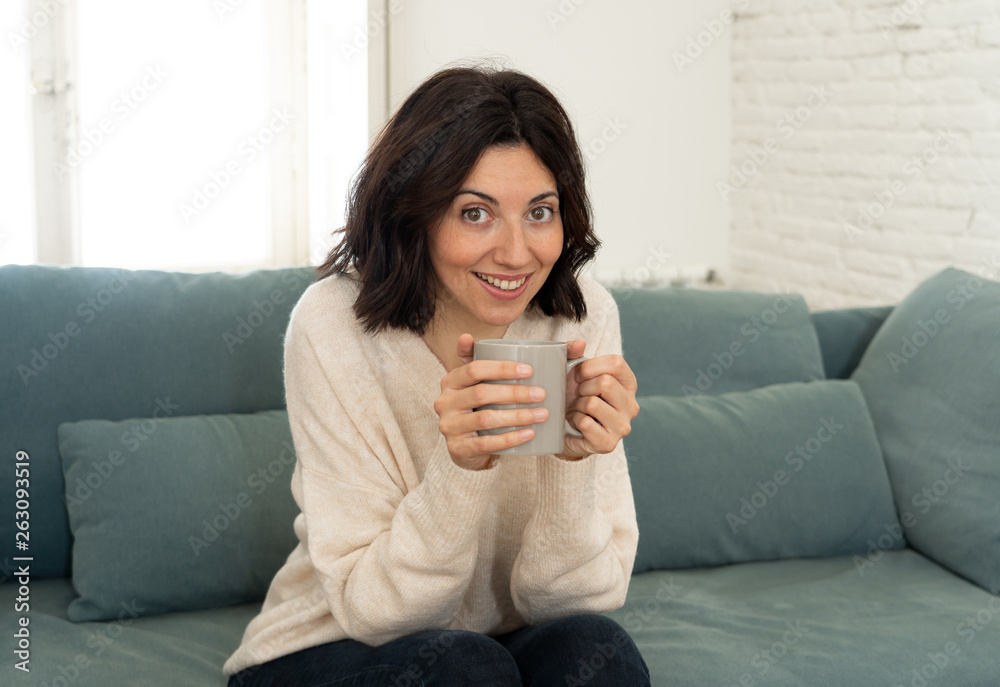 Happy young woman sitting on sofa at home with a hot beverage. In leisure and spare time concept Happy young woman sitting on sofa at home with a hot beverage. In leisure and spare time concept