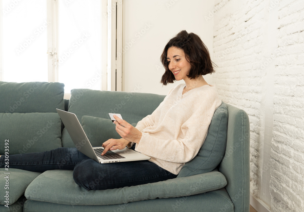 Happy young woman sitting with laptop and a credit card shopping online at home Happy young woman sitting with laptop and a credit card shopping online at home
