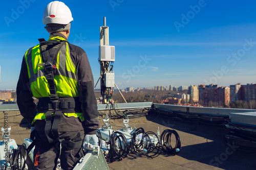 Professional industrial climber in helmet and uniform with telecomunication equipment in his hand and antennas of GSM DCS UMTS LTE bands, outdoor radio units on the roof. Working process of upgrading photo