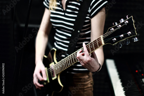 A girl in a striped shirt with an electric guitar stands on the recording Studio. The guitarist plays the strings of a musical instrument. Acoustic background with soundproofing