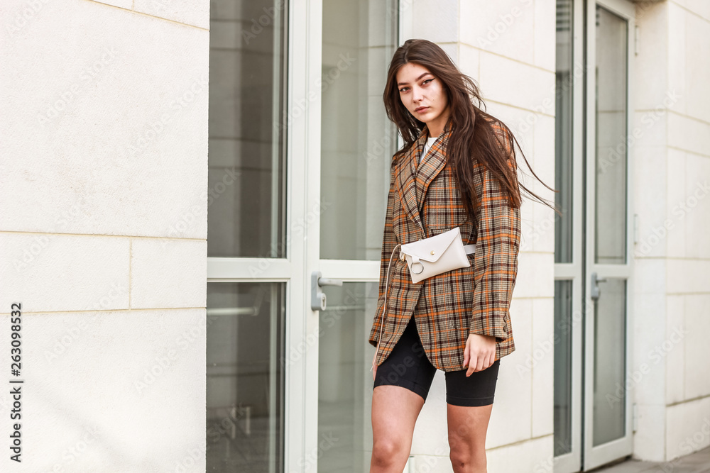 Portrait shooting of a stylish girl. Beige shades. Trends of spring and summer 2019. Wide jacket and belt leather bag. White sneakers and bike shorts Portrait shooting of a stylish girl. Beige shades. Trends of spring and summer 2019. Wide jacket and belt leather bag. White sneakers and bike shorts