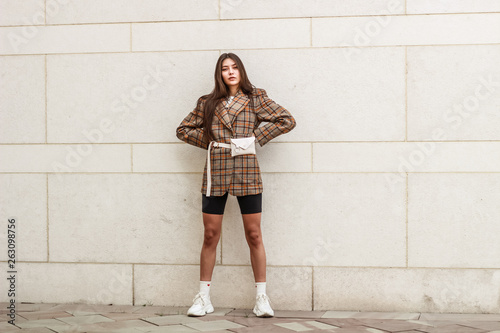 Portrait shooting of a stylish girl. Beige shades. Trends of spring and summer 2019. Wide jacket and belt leather bag. White sneakers and bike shorts