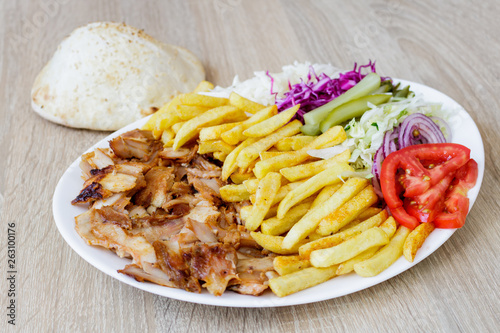 Chiken Doner Kebab on the plate with bread, french fries, tomatoes, onion, pickles and salad on a wooden background. Grilled chicken meat with vegetables.