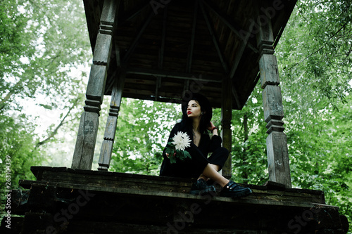 Sensual girl all in black, red lips and hat. Goth dramatic woman hold white chrysanthemum flower.