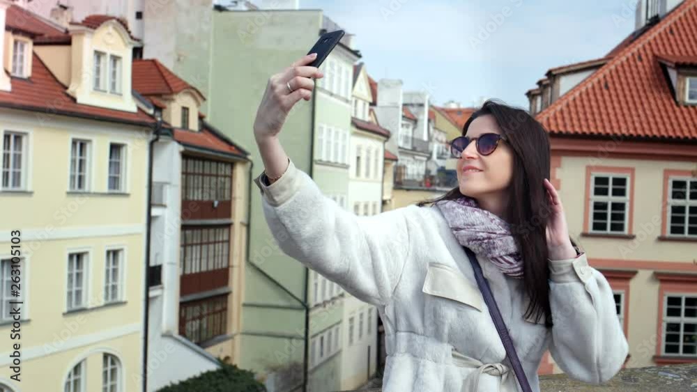 Attractive smiling tourist woman making selfie using smartphone surrounded by city street building Attractive smiling tourist woman making selfie using smartphone surrounded by city street building