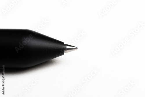 A macro shot of a minimalist barrel ballpoint pen with selective focus on the writing tip set on a plain white background.