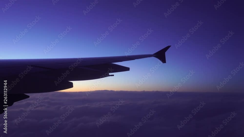 Wing of airplane flying above the clouds in the sky with sunset Wing of airplane flying above the clouds in the sky with sunset