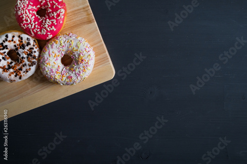 White, pink and brown glazed donuts in left side on black wooden background.