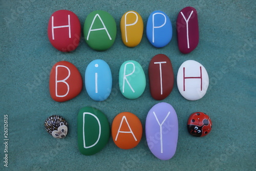 Funny happy birthday postcard idea with colored stone letters and ornamental stone objects over green sand  photo