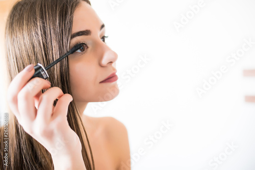 Woman applying black mascara on eyelashes with makeup brush. Young beautiful woman applying mascara makeup on eyes at bathroom. Beautiful brunette girl applying makeup on eyes in the morning time.