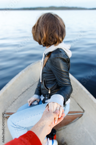 Follow me to the boat on lake. Brunette woman with short hair, black leather jacket holding boyfriend's hand, soft focus. Traveling together with girlfriend.  