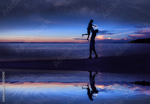 Mirror reflection of Silhouette father and daughter on the beach with million stars galaxy and blue sky early morning.