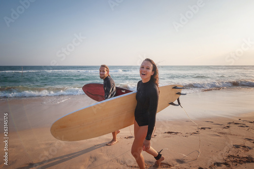 Young couple of happy smiling surfers on ocean coast, sport active lifestyle vacation travel concept