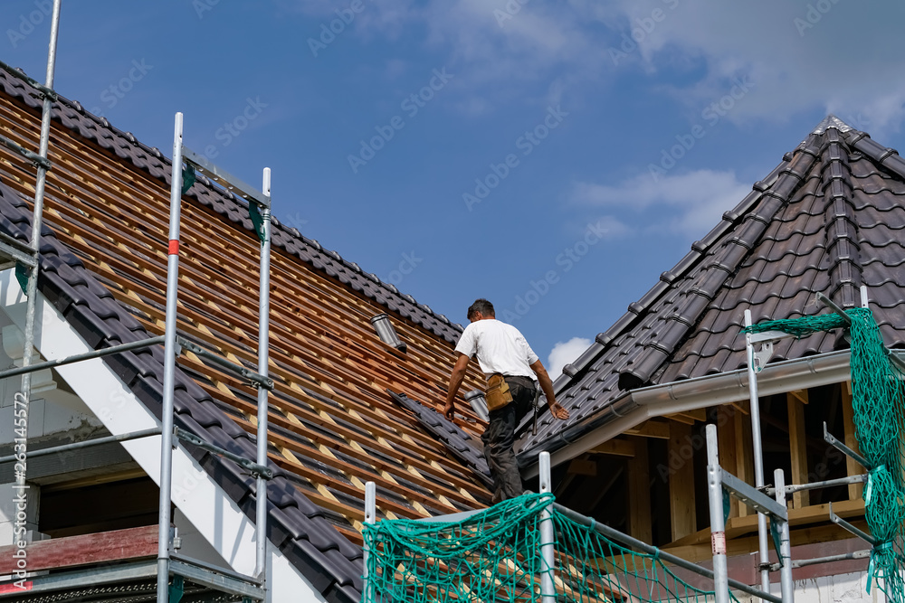 Dachziegel werden durch einen Dachdecker auf einen Neubau befestigt Dachziegel werden durch einen Dachdecker auf einen Neubau befestigt
