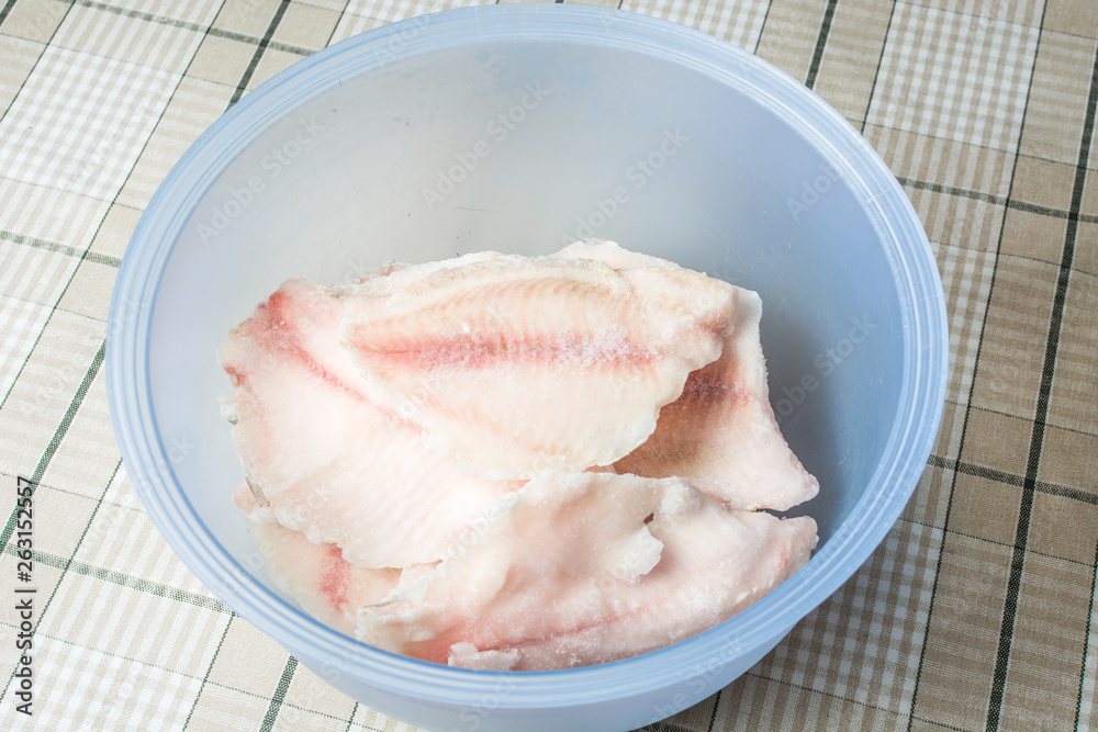 Frozen tilapia fish in deep defrosting bowl. Frozen tilapia fish in deep defrosting bowl.