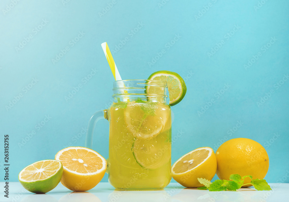 Lemonade drink of soda water, citrus and mint on the light blue background. Cocktail glass with handle and straw, sliced lemon and lime, front view Lemonade drink of soda water, citrus and mint on the light blue background. Cocktail glass with handle and straw, sliced lemon and lime, front view