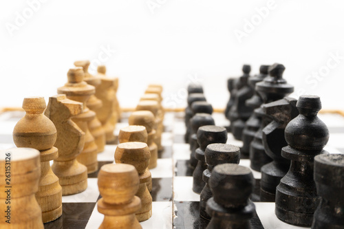 two sides of black and white chess pieces  which are made of wood  are facing each other. There is a white background for placing posts