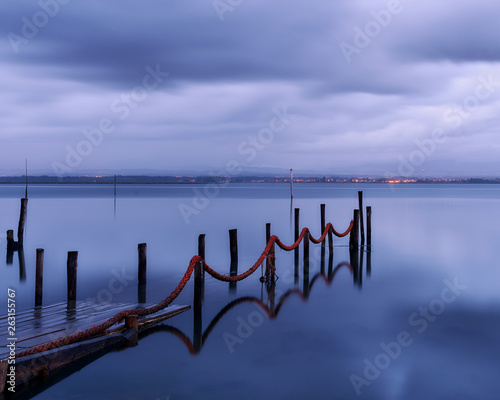 Palafitic pier submerged by the high tide at end of day, only the poles are visible. Blue hour witna tint of orange in the clouds. photo