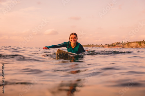 Surfgirl with perfect body on a surfboard floating in ocean. Surfing at sunset