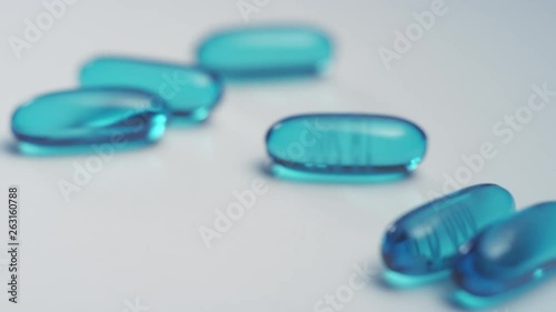 Macro close-up rack focus on blue ibuprofen liquid gel pills scattered on a white surface