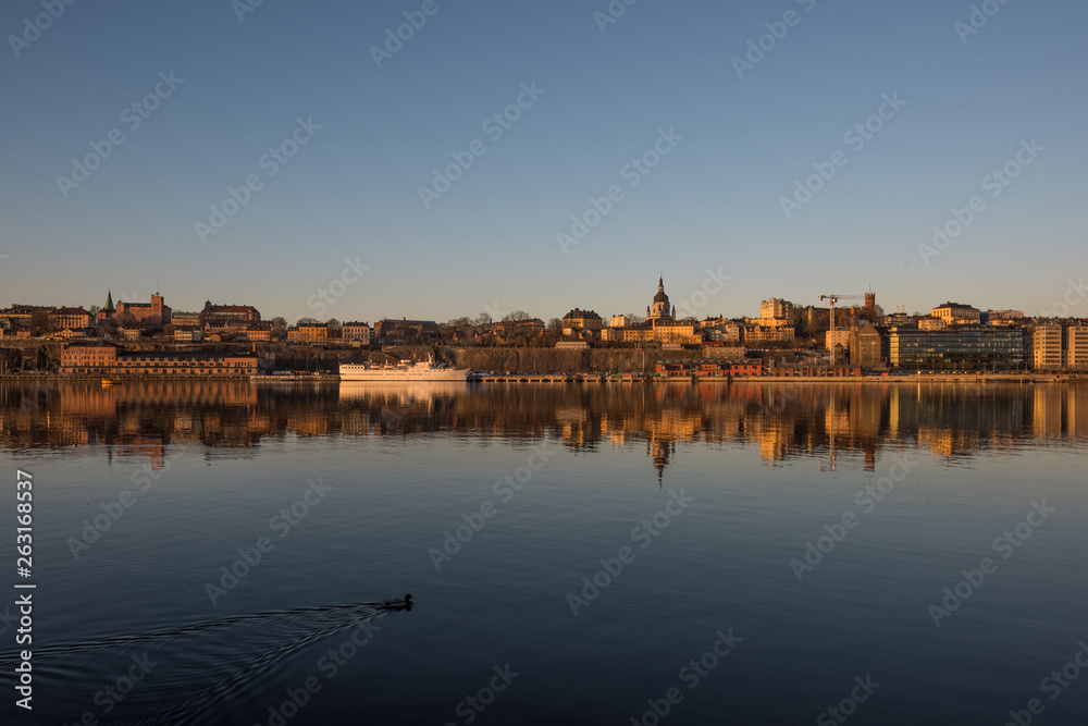 A sunny early spring day in Stockholm, view over a pier with boats and birds at the old town and the Södermalm district 