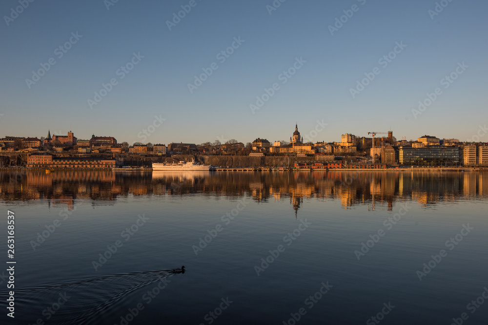 A sunny early spring day in Stockholm, view over a pier with boats and birds at the old town and the Södermalm district A sunny early spring day in Stockholm, view over a pier with boats and birds at the old town and the Södermalm district