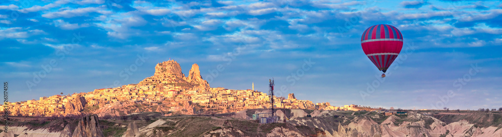 Panoramic view of the Turkish fortress Uchisar in the morning and one hot air balloon, landscape of Goreme in Cappadocia, Turkey.