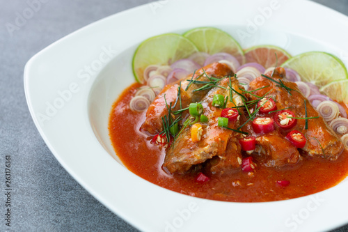 Spicy sardine salad with tomato sauce in white dish on concrete table.