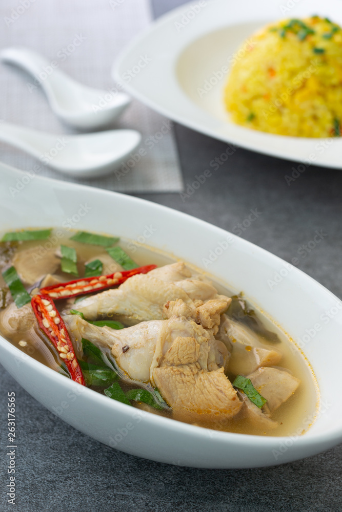 Sour and spicy soup with chicken drumstick and in white bowl and fried rice with turmeric in white dish on concrete table. Sour and spicy soup with chicken drumstick and in white bowl and fried rice with turmeric in white dish on concrete table.