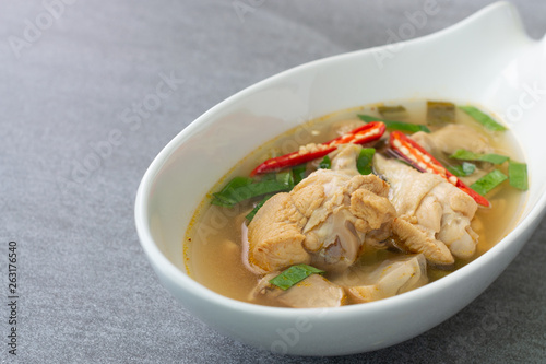 Sour and spicy soup with chicken drumstick in white bowl on concrete table.