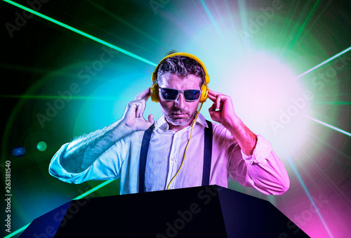 young attractive and cool DJ in shirt and suspenders remixing music at night club using headphones in party strobo and laser lights background in clubbing and nightlife © TheVisualsYouNeed