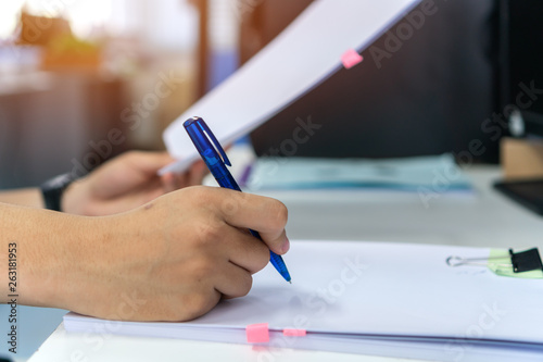 Document report and business busy concept: Businessman manager hands holding blue pen for reading and signing in paperwork or documentation files on computer modern corporate office background.