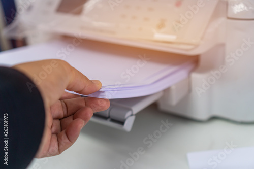 Printer or printing documents in office concept: Businessman press white paper in laser printed cartridge feeder, scanner machine for copy document to report in busy modern offices background