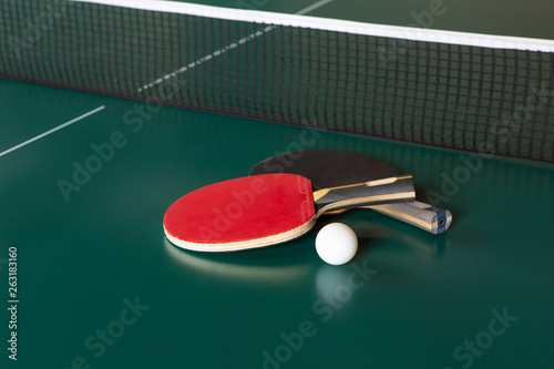 two ping-pong rackets and a ball on a green table. ping-pong net.