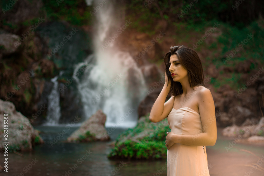 Sexy woman posing on the rock among green tropical plants and beside beautiful waterfall with blue water. Fairy tale. Sexy woman posing on the rock among green tropical plants and beside beautiful waterfall with blue water. Fairy tale.