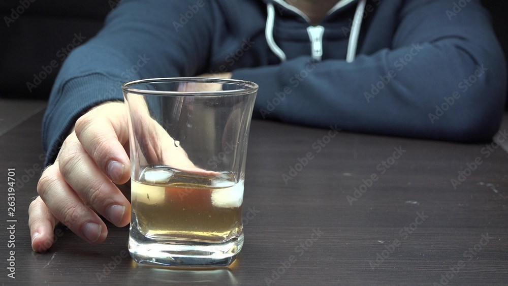 Man hand holding a glass with alcohol on a table, drinking Man hand holding a glass with alcohol on a table, drinking