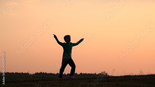 Happy child silhouette playing, singing, dancing, moving hands close sunset colorful sky, symbol of joyful childhood, concept of freedom, gorgeous nature