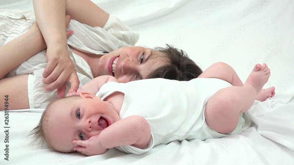 Portrait of attractive young mother and lovely baby with blue eyes, smiling face, blue, laying down on bed and holding hands, pure love Portrait of attractive young mother and lovely baby with blue eyes, smiling face, blue, laying down on bed and holding hands, pure love