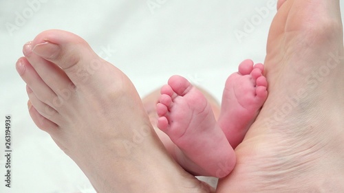Newborn baby feet between mother feet, conceptual, secure shelter © MEDIAIMAG