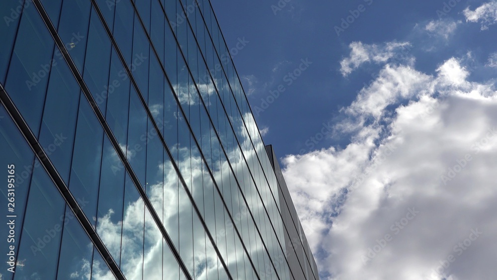 Fluffy white clouds on blue sky mirrored in modern glass building