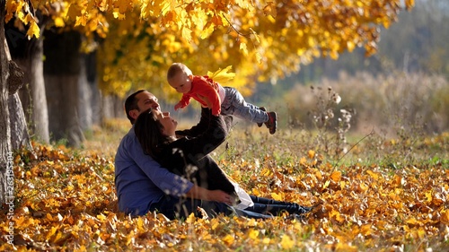 Portrait of young family in autumn park, parents play with baby, sunny day
